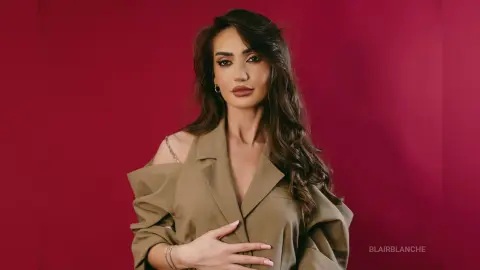 Elegant woman in a stylish beige blazer posing against a deep red background with a sophisticated mood.