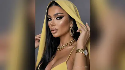 Glamorous woman in a yellow headscarf and gold jewelry posing with elegant makeup against a grey background.
