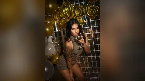 Glamorous woman in a sparkly gold cocktail dress holding a champagne glass at a celebratory New Year's Eve party.