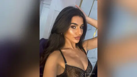 Glamorous woman with long dark hair wearing a black lace bra in a bright, modern indoor setting.