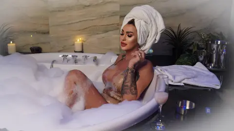 Relaxed woman in a gold bikini relaxing in a bubble bath with a towel wrap in a luxury spa setting.
