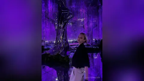 Blonde woman in a black shirt standing before a magical purple glowing light installation in a dreamy setting.