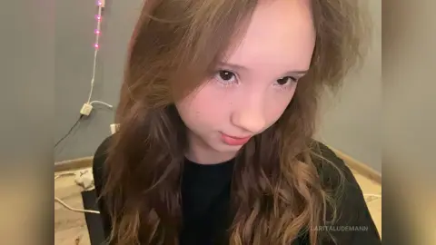 LaritaLudemann looks into the camera with long wavy brown hair while wearing a black top.