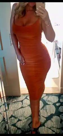 Woman in a burnt orange bodycon midi dress posing in a bright room for a mirror selfie.