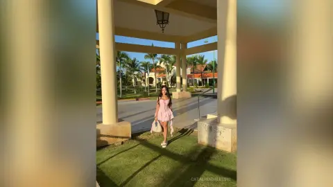 Stylish woman in a pink mini dress standing under a sunny tropical resort pavilion.