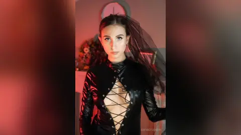 Woman in black lace-up bodysuit and dark veil posing in moody red lighting.