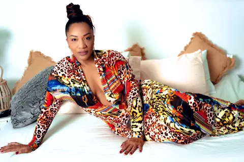 Elegant woman in a colorful leopard print maxi dress lounging on a white bed in a bright, cozy bedroom.