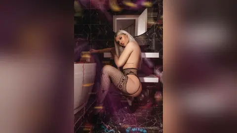 Glamorous blonde woman in black fishnet lingerie sitting in a luxury marble bathroom.