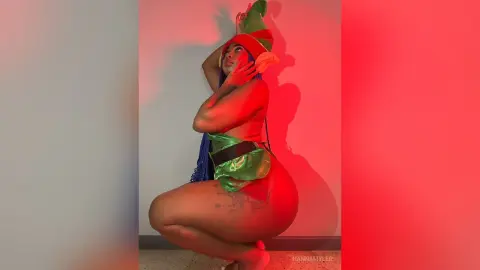 Curvy woman in a green elf costume posing under moody red lighting for a festive holiday photoshoot.