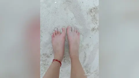 Close-up of bare feet resting on soft white sand at a peaceful summer beach.