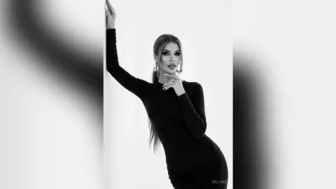 Elegant woman in a black long-sleeve dress posing glamorously against a minimalist white background.