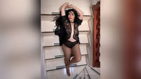 Elegant woman in black lace lingerie relaxing on white stairs in a moody, high-angle pose.