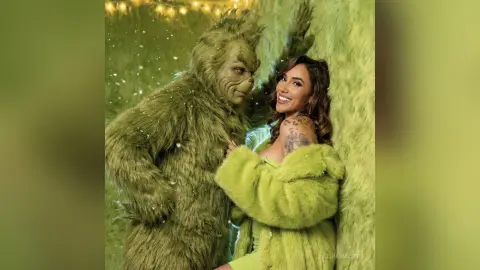 Smiling woman in a lime green faux fur coat posing with the Grinch character in a festive snowy setting.