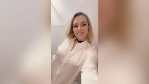 Smiling blonde woman in a white button-down shirt posing in a bright, minimalist indoor setting.