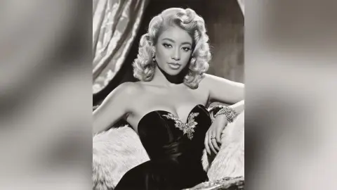 Elegant woman in a black velvet strapless gown with vintage wavy hair posing glamorously in a classic studio setting.