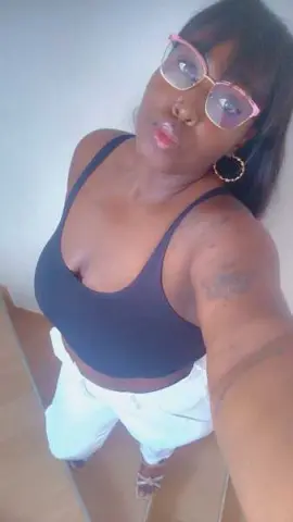 Young woman in a black tank top and white pants posing for a casual indoor selfie.