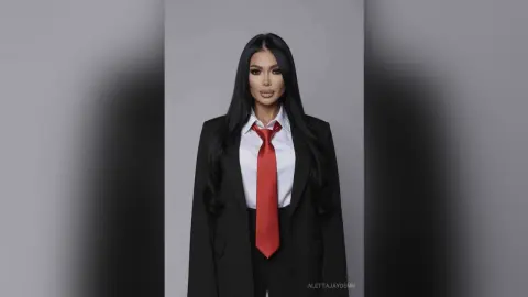 Elegant woman in a black blazer and red tie posing confidently against a grey studio background.