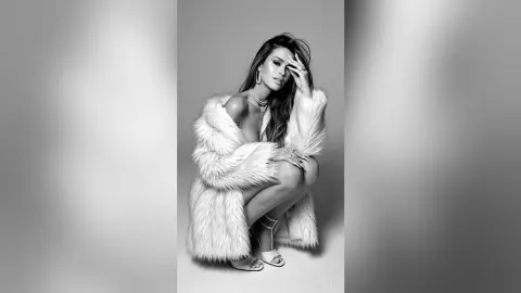 Elegant woman in a white faux fur coat posing glamorously in a studio setting.