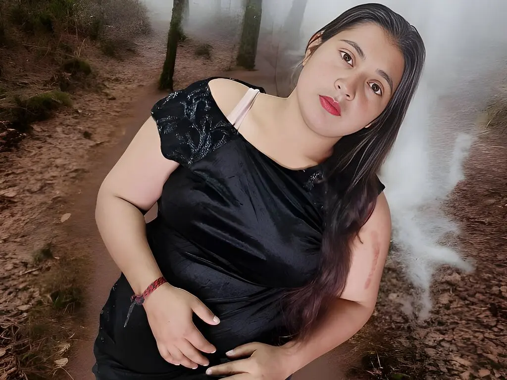Smiling woman in a black dress posing on a misty forest path during a moody outdoor photoshoot.