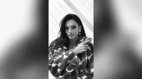 Elegant woman in a patterned faux fur coat posing with a sophisticated mood in a black and white portrait.
