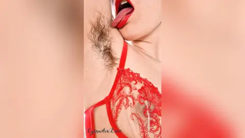 Woman in red lace lingerie showing natural underarm hair in a sensual, intimate close-up shot.