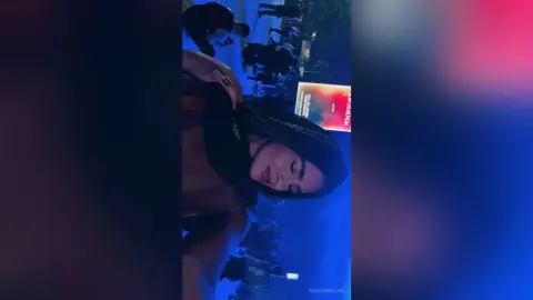 Young woman in a black top smiling during a vibrant nighttime outdoor event with blue ambient lighting.