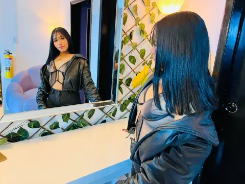 Young woman in a black leather jacket and crop top taking a moody mirror selfie in a bright room.