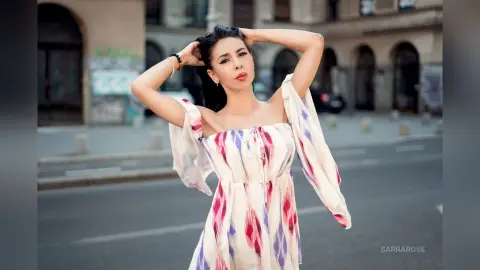 Stylish woman in a white and purple patterned sundress posing on a city street during golden hour.