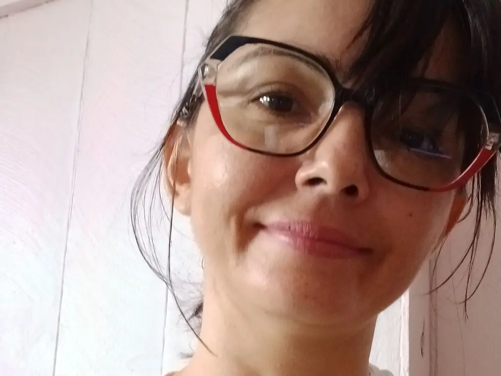 Smiling woman with dark hair and stylish black-rimmed glasses in a bright indoor setting.