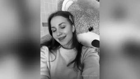 MargaritaHafele smiles while leaning against a large teddy bear, wearing a light-colored sweater with her long hair down.