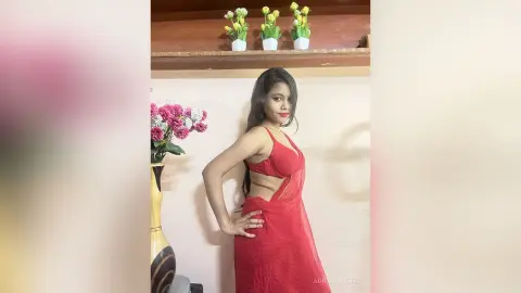 AdrianaReyez poses in a red dress with a cut-out waist, looking over her shoulder with long dark hair and red lipstick.