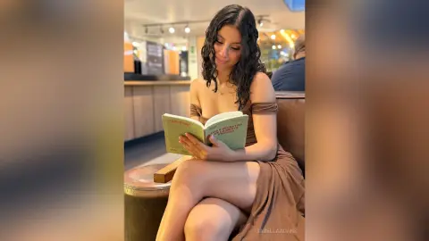 Young woman in a brown dress reading a book in a cozy cafe setting.