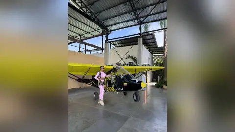 Aleja stands next to a small yellow airplane, wearing a pink tank top and pink leggings.
