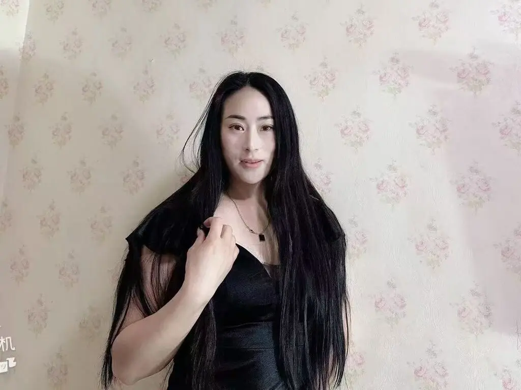 Young woman with long black hair wearing a black velvet dress against a floral wallpaper background.