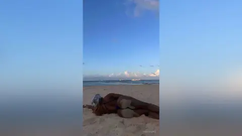 A woman in a bikini relaxing on a sunny tropical beach under a clear blue sky.