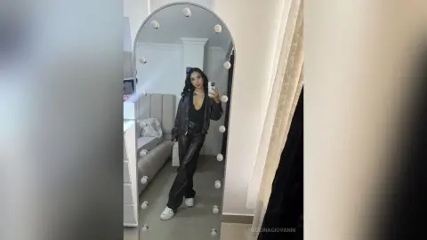 Stylish woman in black leather jacket and trousers taking a selfie in a modern bedroom mirror.