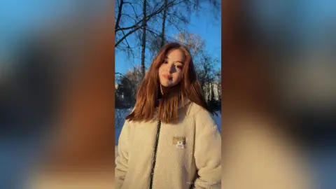 PaulettaRerucha poses outdoors against a blue sky and trees, wearing a white zip-up fleece jacket.