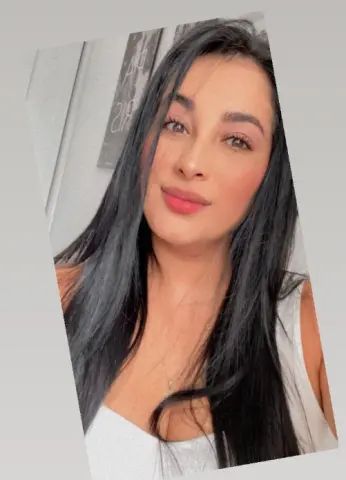 Smiling young woman with long dark hair wearing a white tank top in a bright indoor setting.
