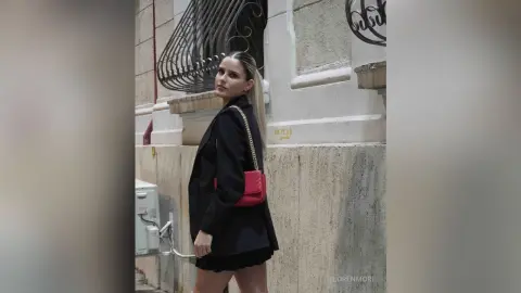 Stylish woman in a black blazer and mini skirt posing against a stone building wall in an urban setting.