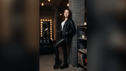 Stylish woman in a black leather jacket and skinny jeans posing in a moody, industrial loft setting.