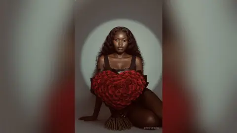 ZoeySpark poses in a black tank top, holding a large heart-shaped arrangement of red roses against her chest in a studio setting.