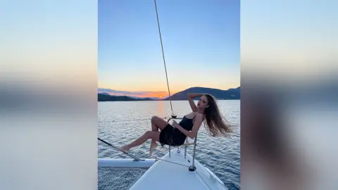EvelynMills reclines on the white deck of a boat at sunset, wearing a black bikini or bodysuit.