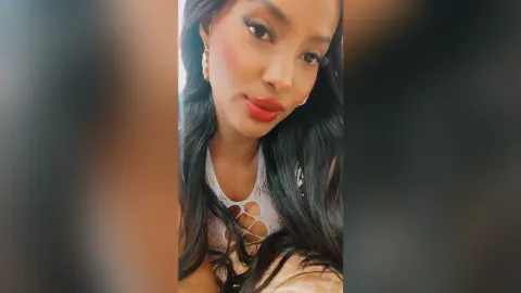 NohomiCambel poses with long dark hair and red lipstick wearing a white lace cutout top.