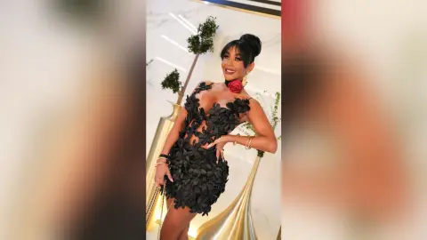 Dolce poses in a short black floral lace dress with a plunging neckline and gold jewelry.