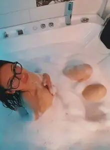 Relaxed woman with glasses enjoying a relaxing bubble bath in a white modern bathtub.