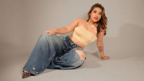 Young woman in a beige tube top and baggy distressed jeans sitting against a grey studio background.