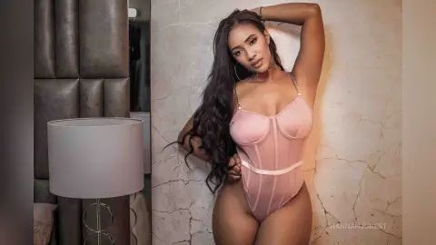 Beautiful woman in a pink corset bodysuit posing against a marble wall in a moody, elegant setting.