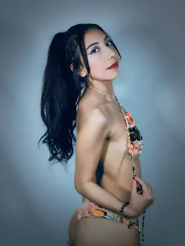 Young woman with long dark hair in a floral bikini posing against a blue studio background.