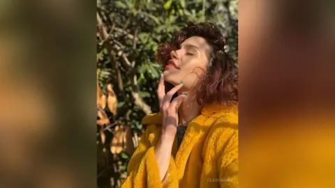 Serene woman in a cozy yellow fleece jacket relaxing in warm sunlight amidst lush green foliage.