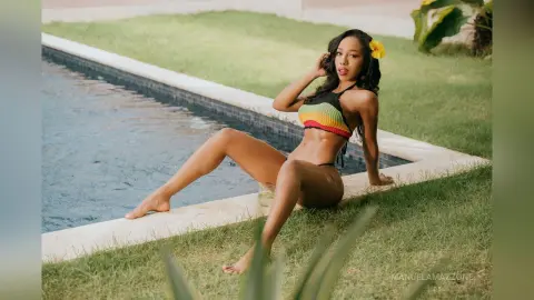 Smiling woman in a colorful crochet bikini relaxing by a backyard swimming pool on a sunny summer day.